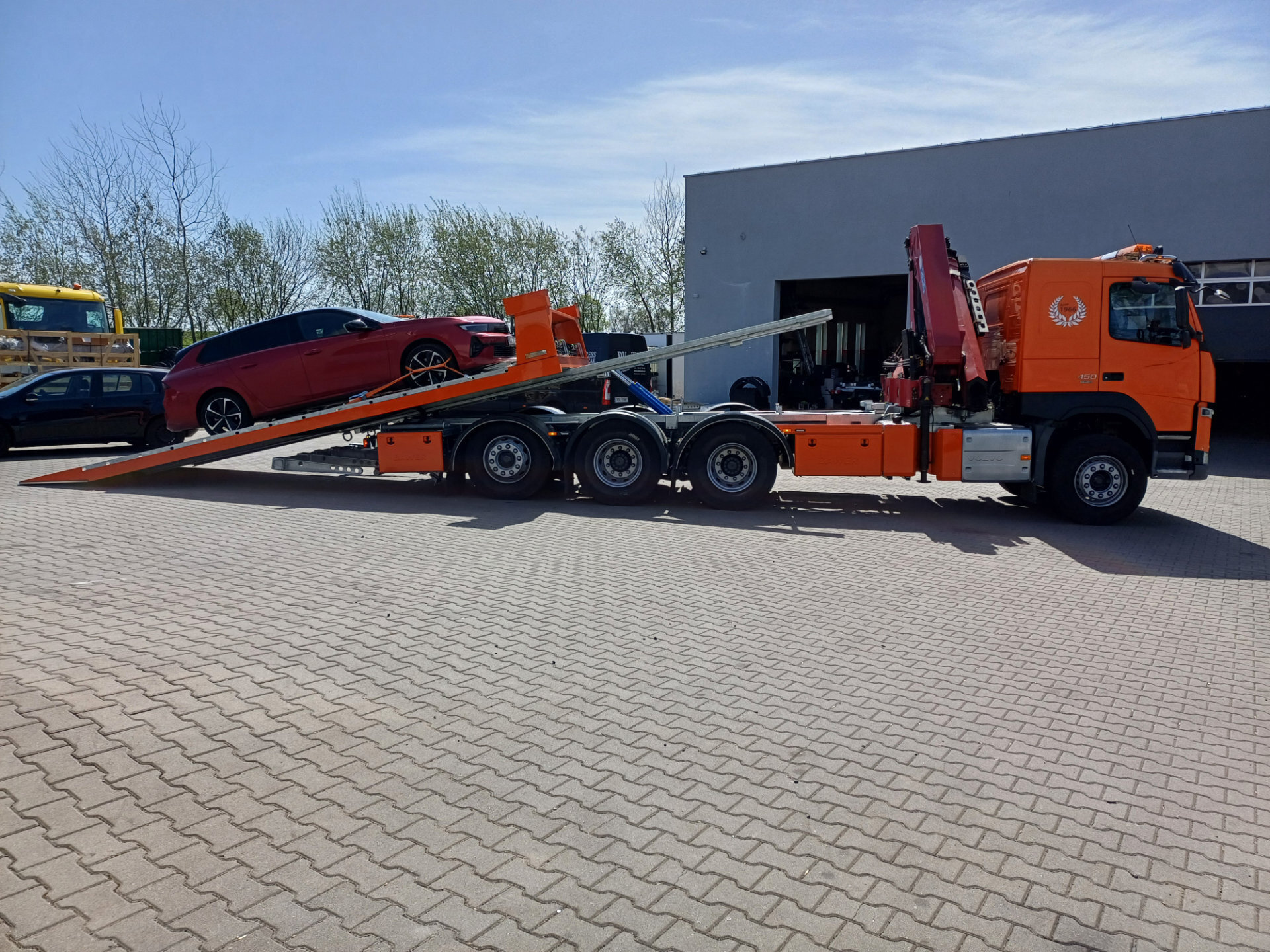 Pomarańczowy Volvo FM 450 z platformą hydrauliczną i samochodem