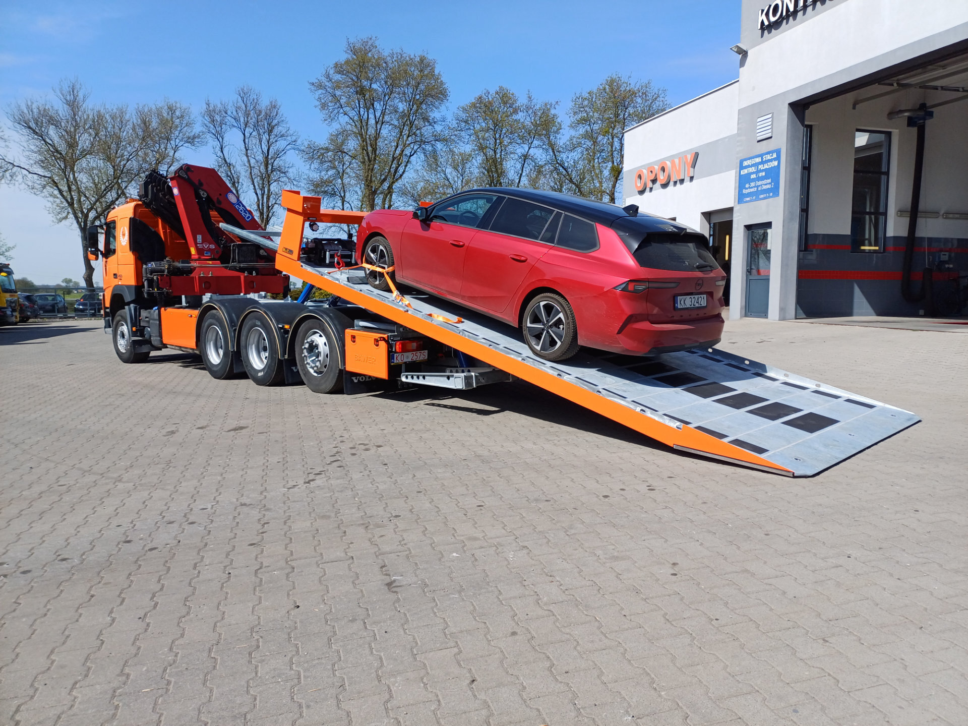 Pomarańczowa laweta Volvo FM 450 z czerwonym samochodem osobowym