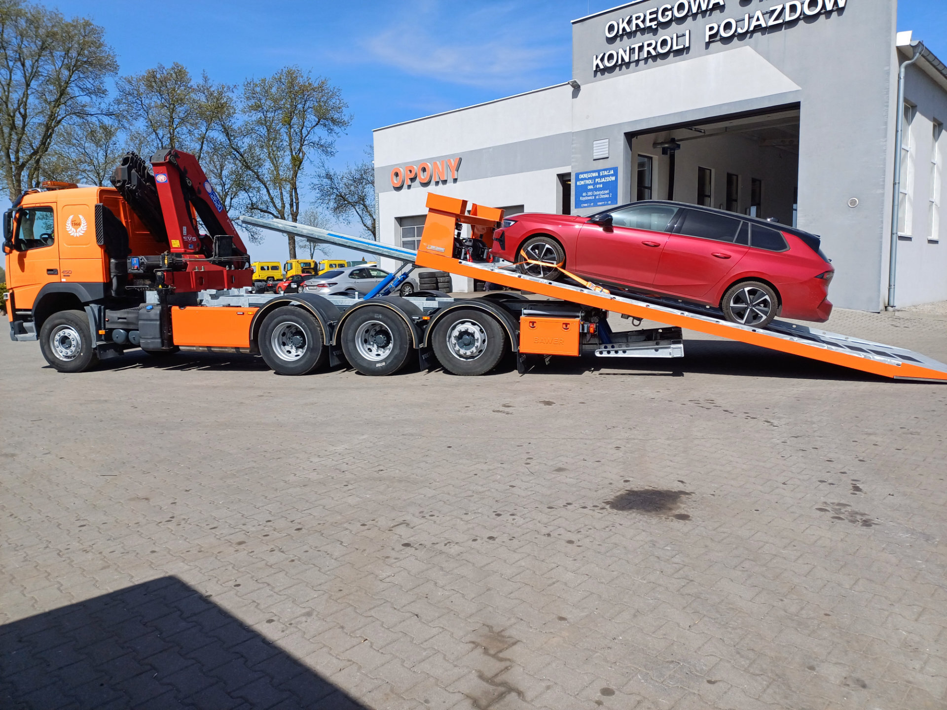 Ciężarówka Volvo z platformą hydrauliczną i czerwonym samochodem.