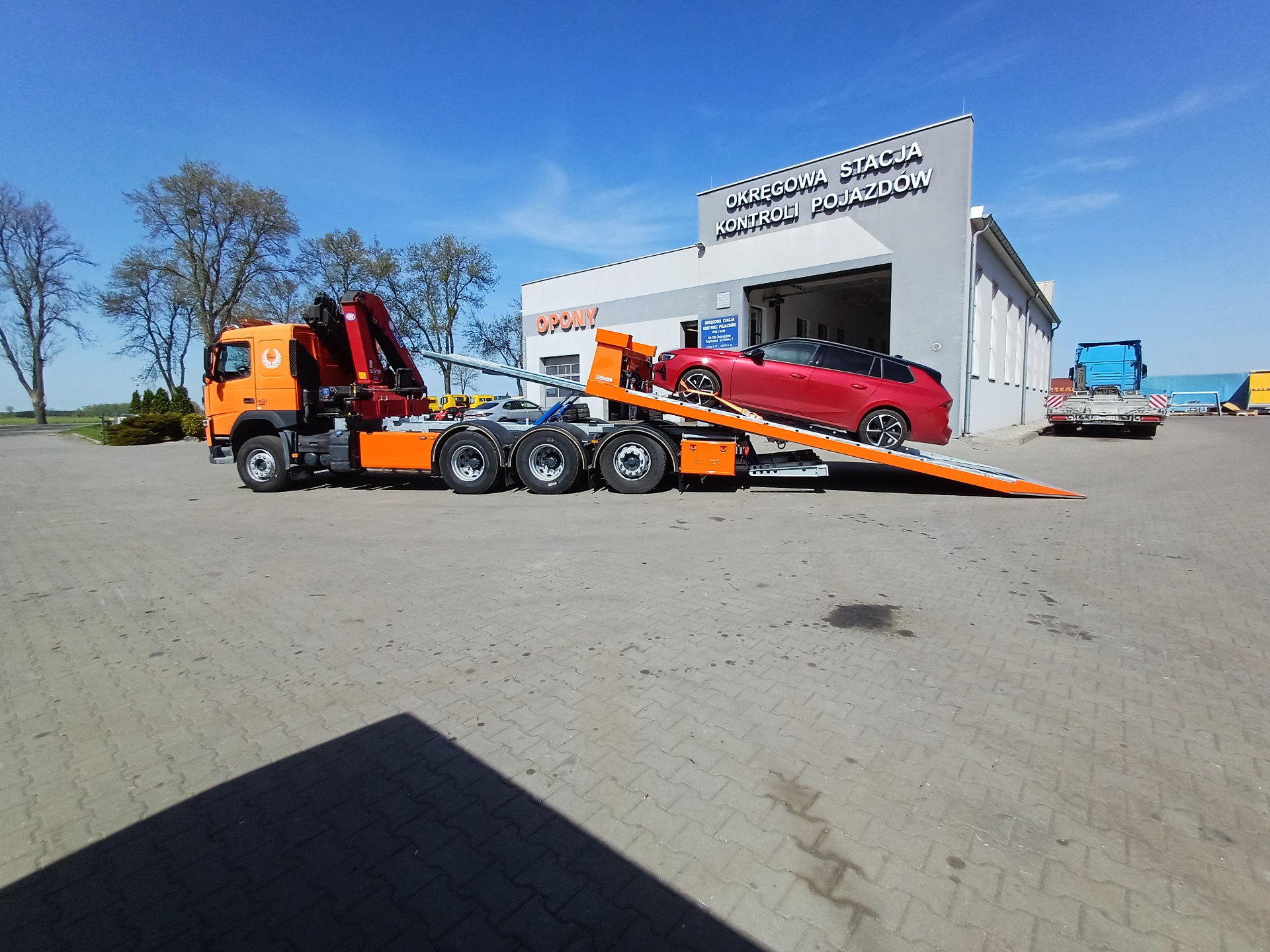 Ciężarówka Volvo z platformą hydrauliczną i czerwonym samochodem.