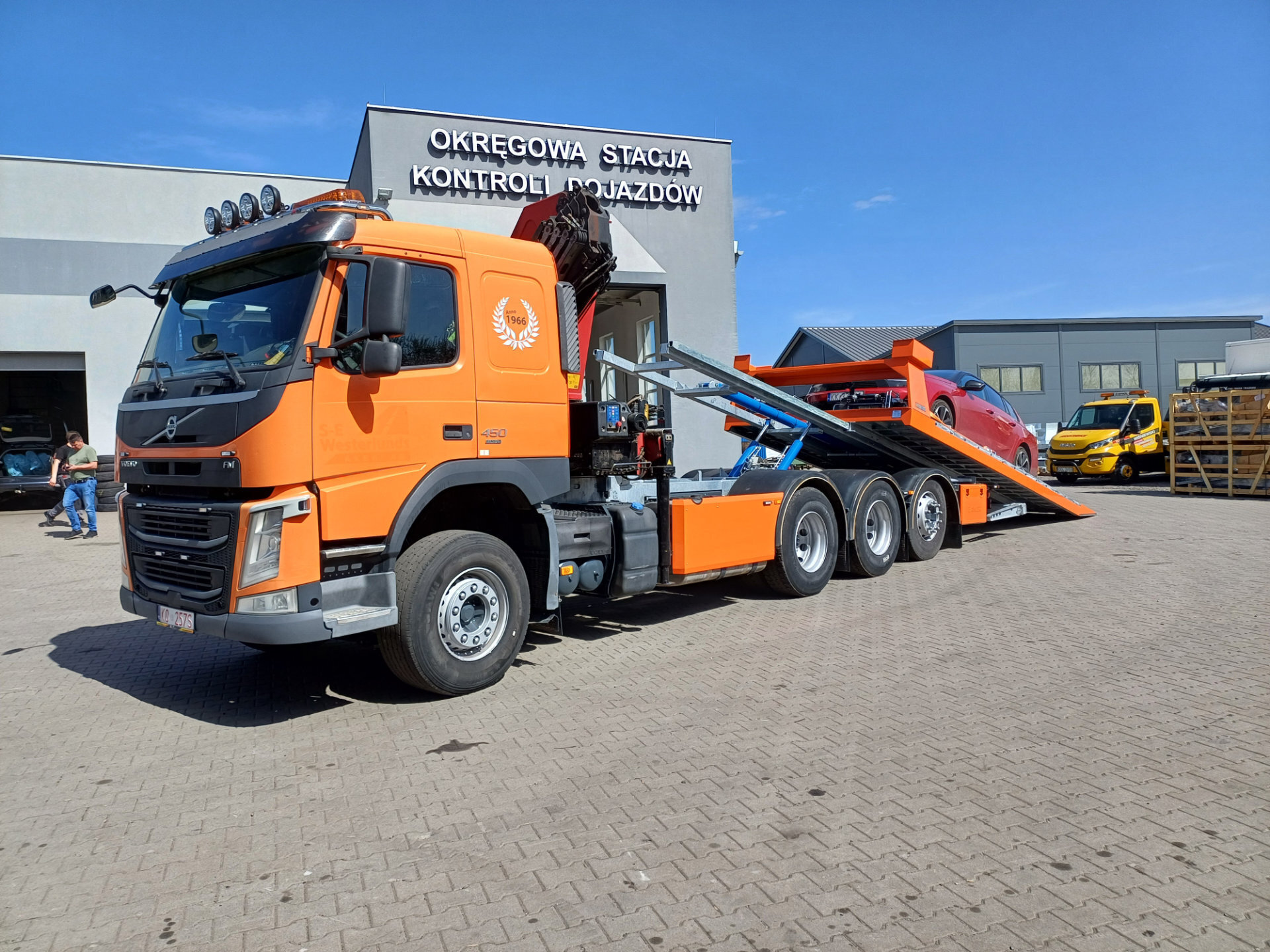 pomarańczowy Volvo FM 450 z platformą hydrauliczną holujący samochód czerwony