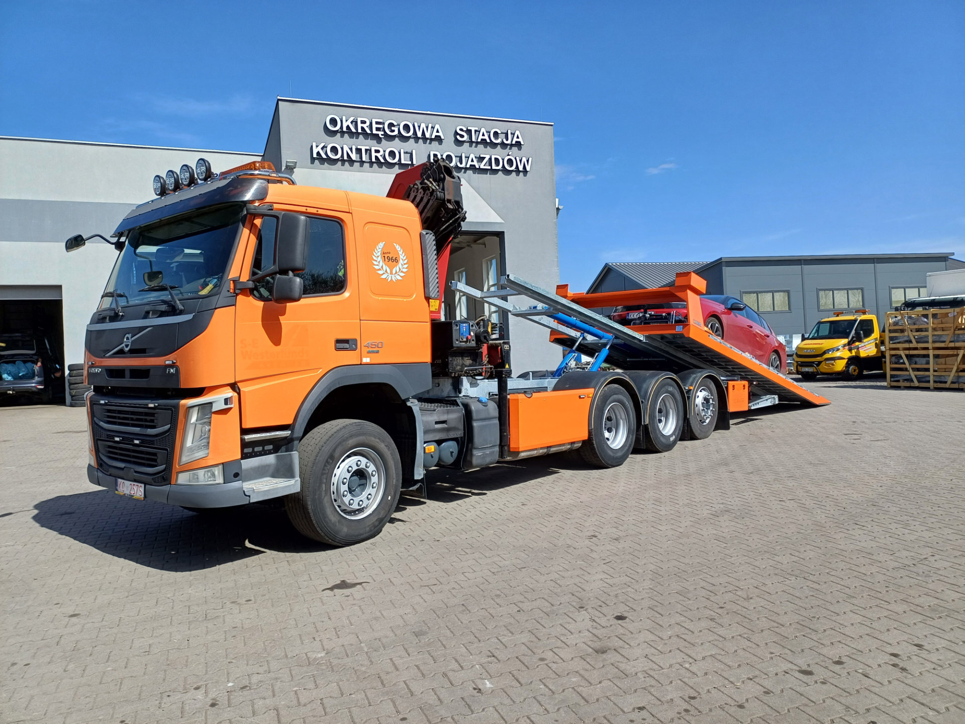 pomarańczowy Volvo FM 450 laweta z czerwoną osobówką