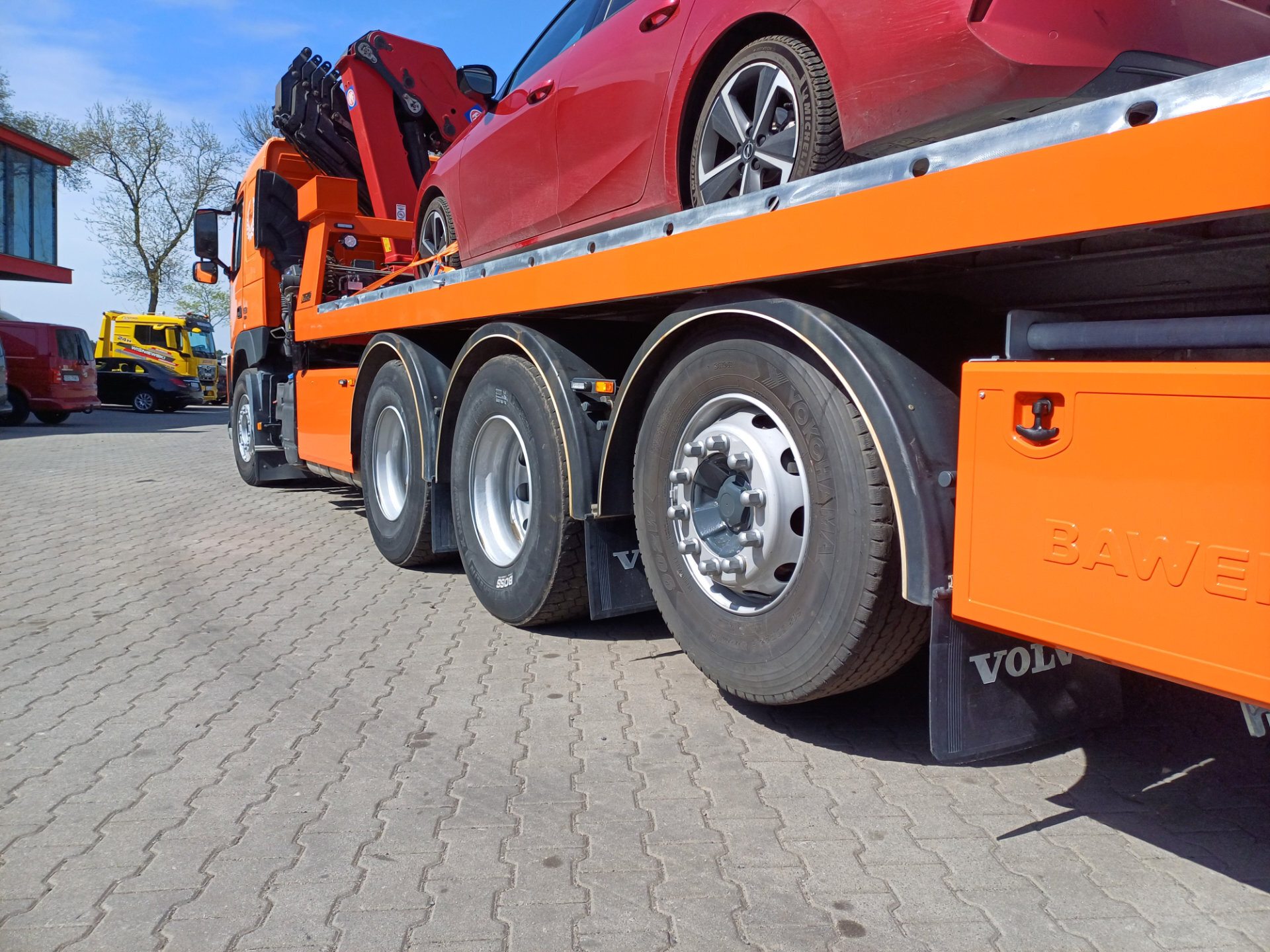 Ciężarówka Volvo z platformą hydrauliczną i czerwonym samochodem.