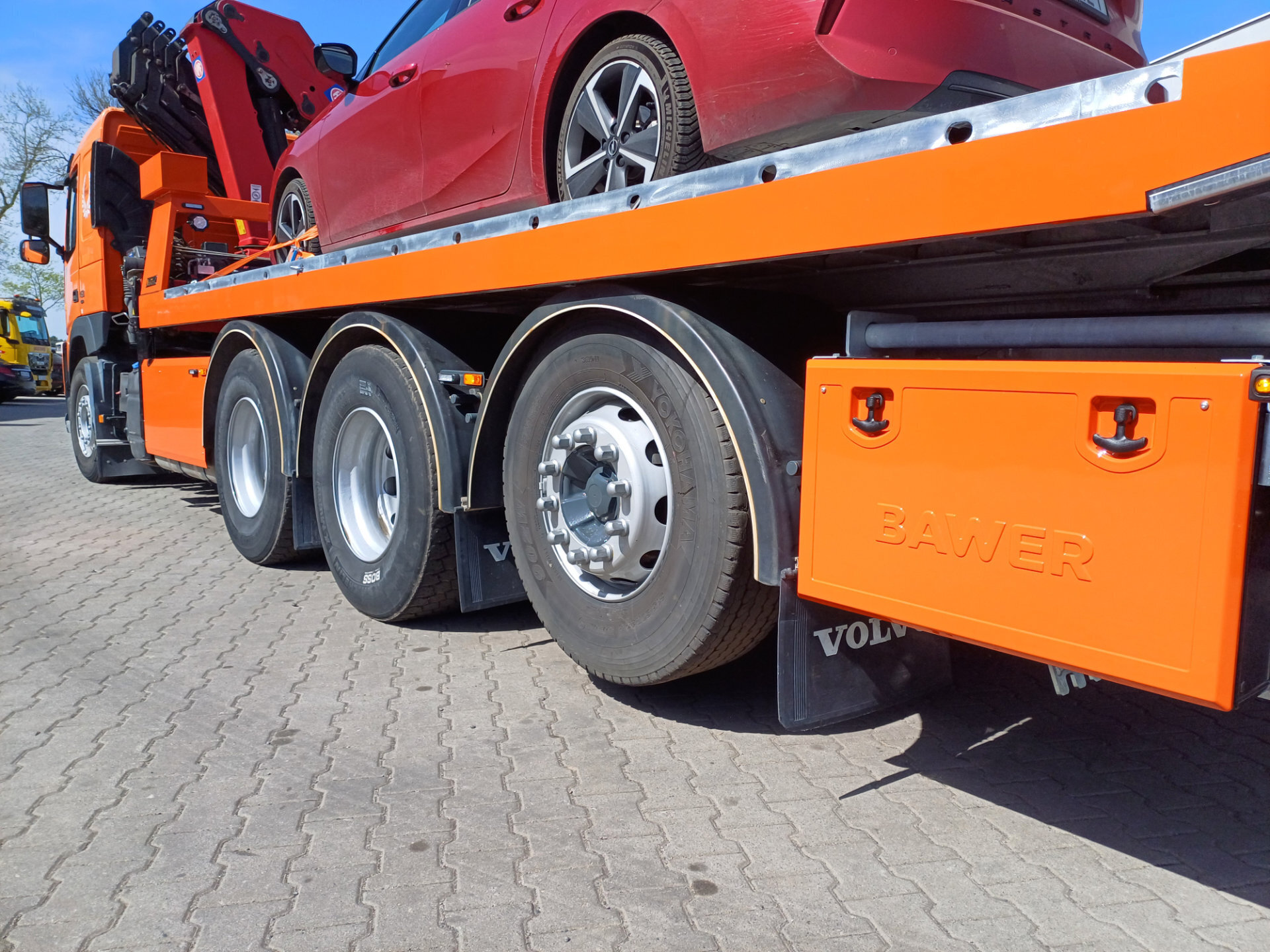 Pomarańczowa laweta Volvo FM 450 z czerwoną osobówką