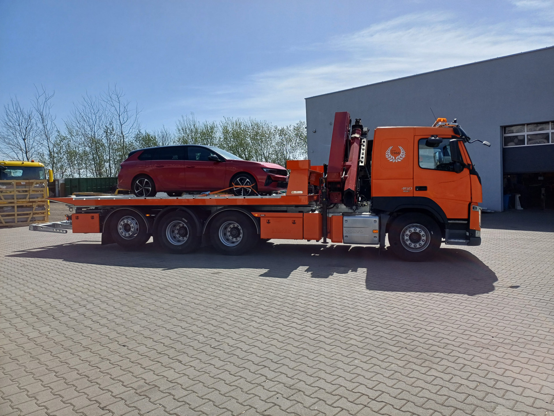 Ciężarówka Volvo FM 450 z platformą hydrauliczną i czerwonym samochodem.