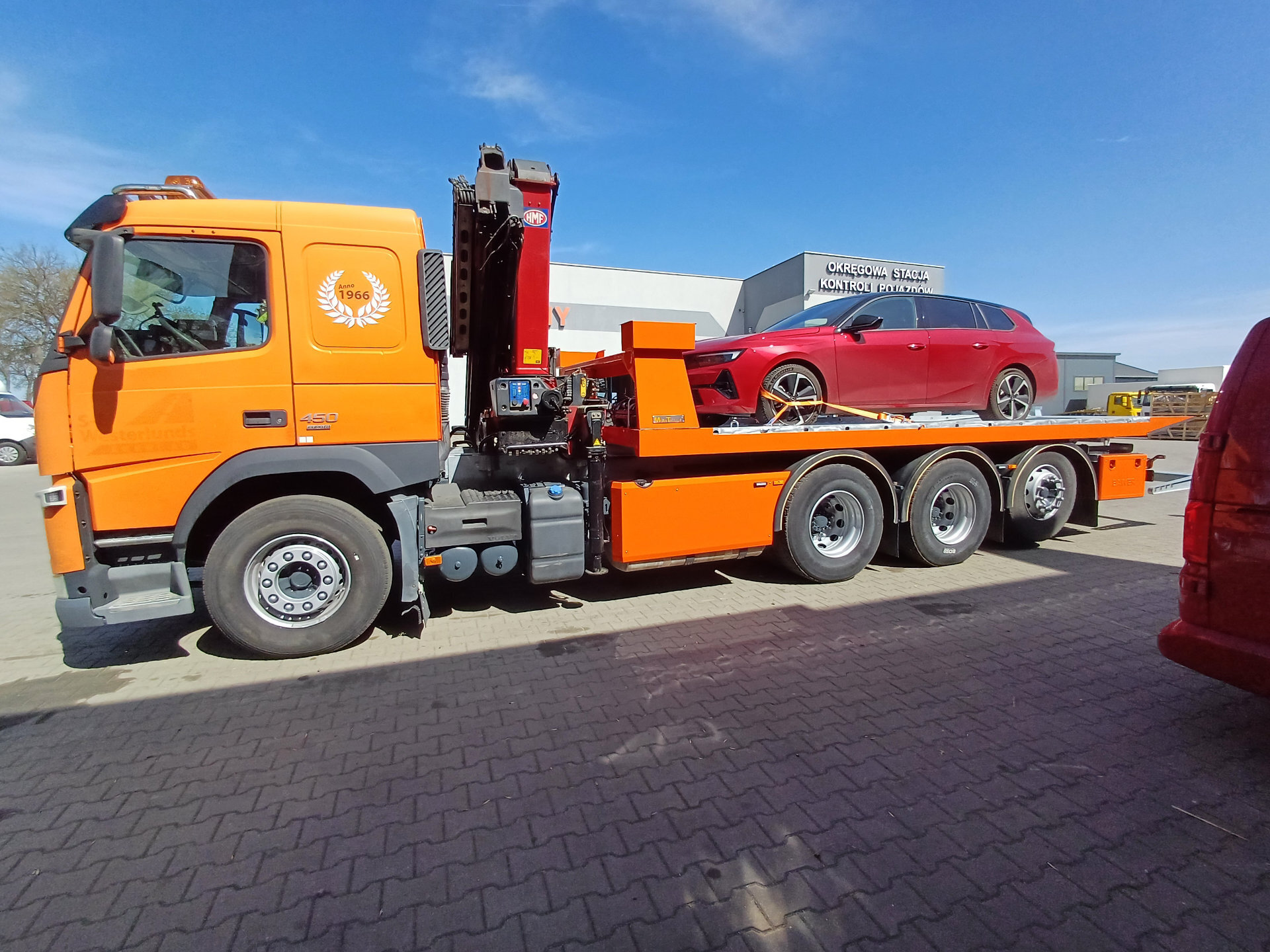 Pomarańczowy Volvo FM 450 z platformą hydrauliczną i samochodem
