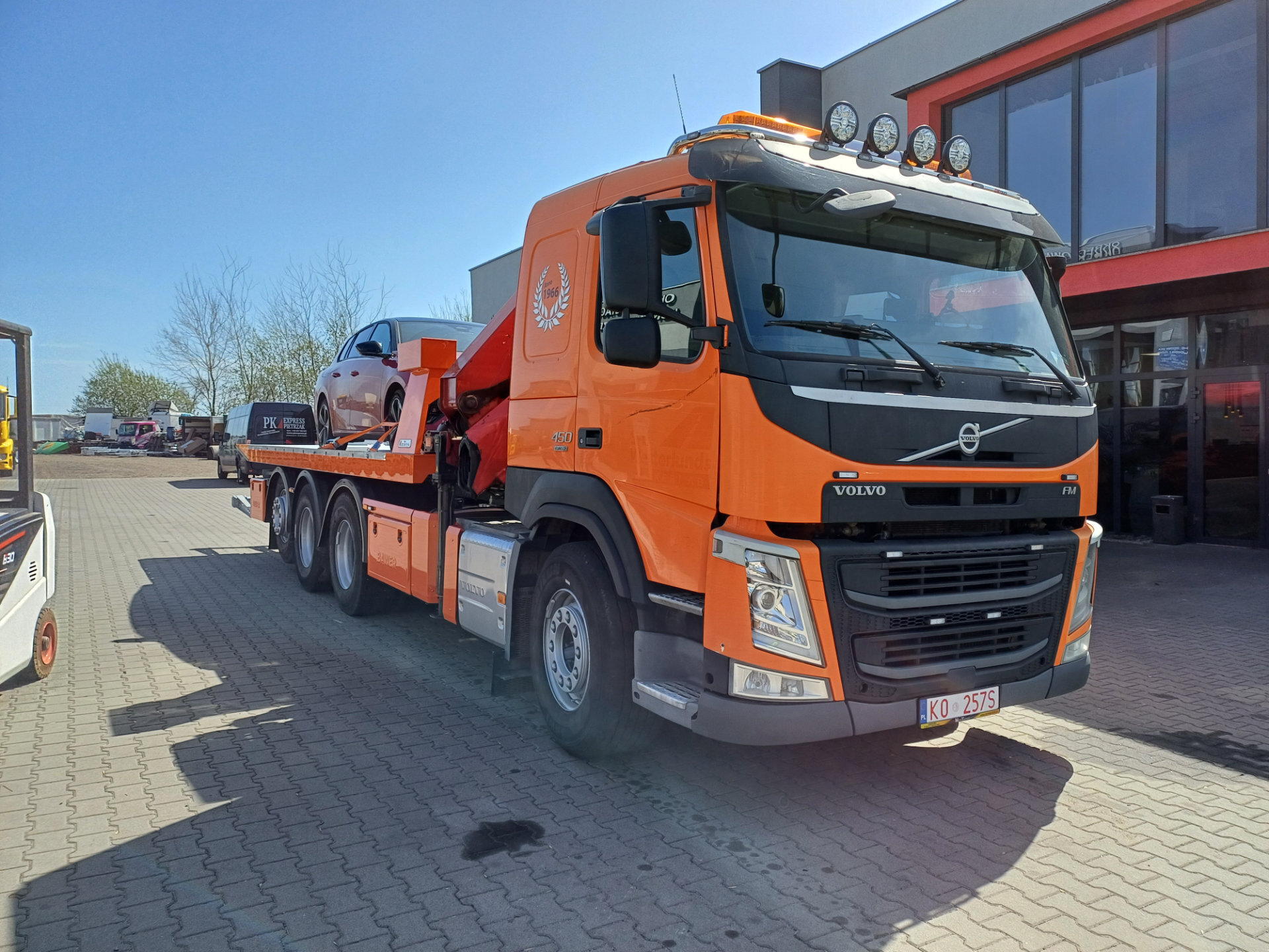 pomarańczowy samochód ciężarowy Volvo holownik z autem na platformie