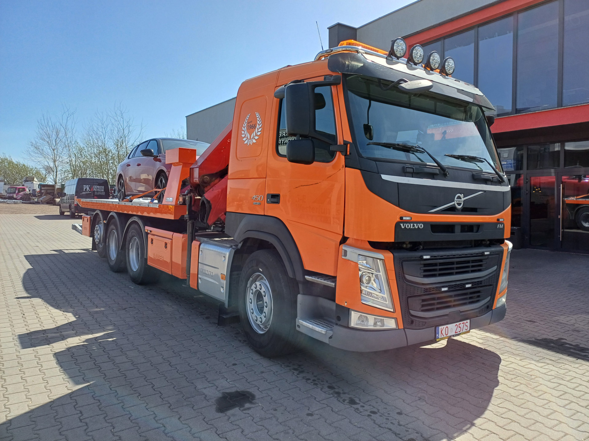 Pomarańczowy Volvo FM 450 z platformą hydrauliczną holujący samochód osobowy