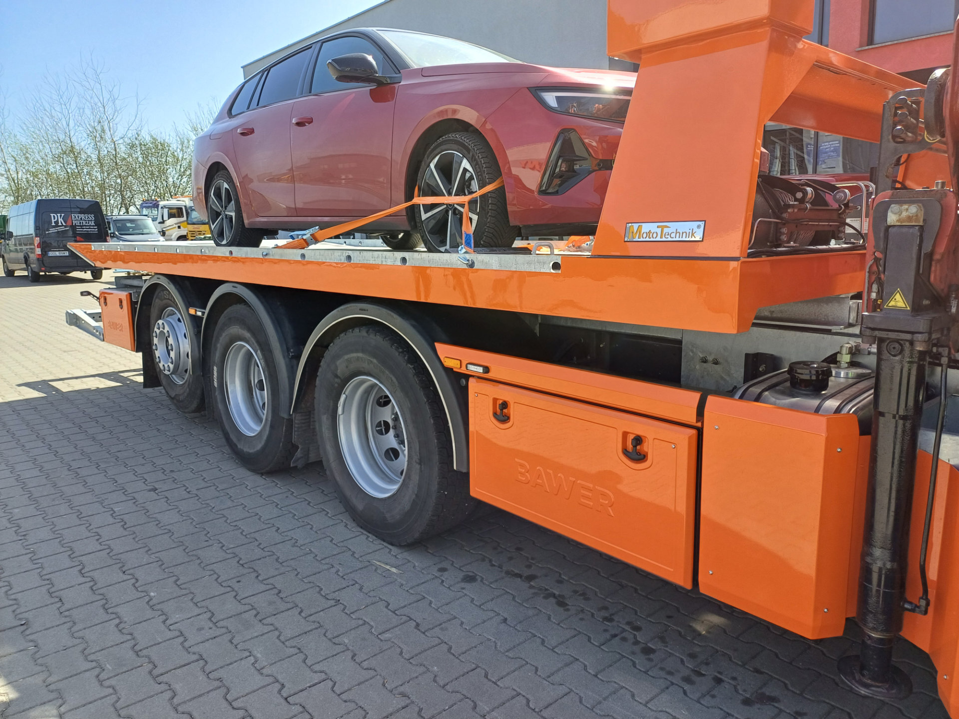 Samochód osobowy na pomarańczowej platformie hydraulicznej Volvo FM 450