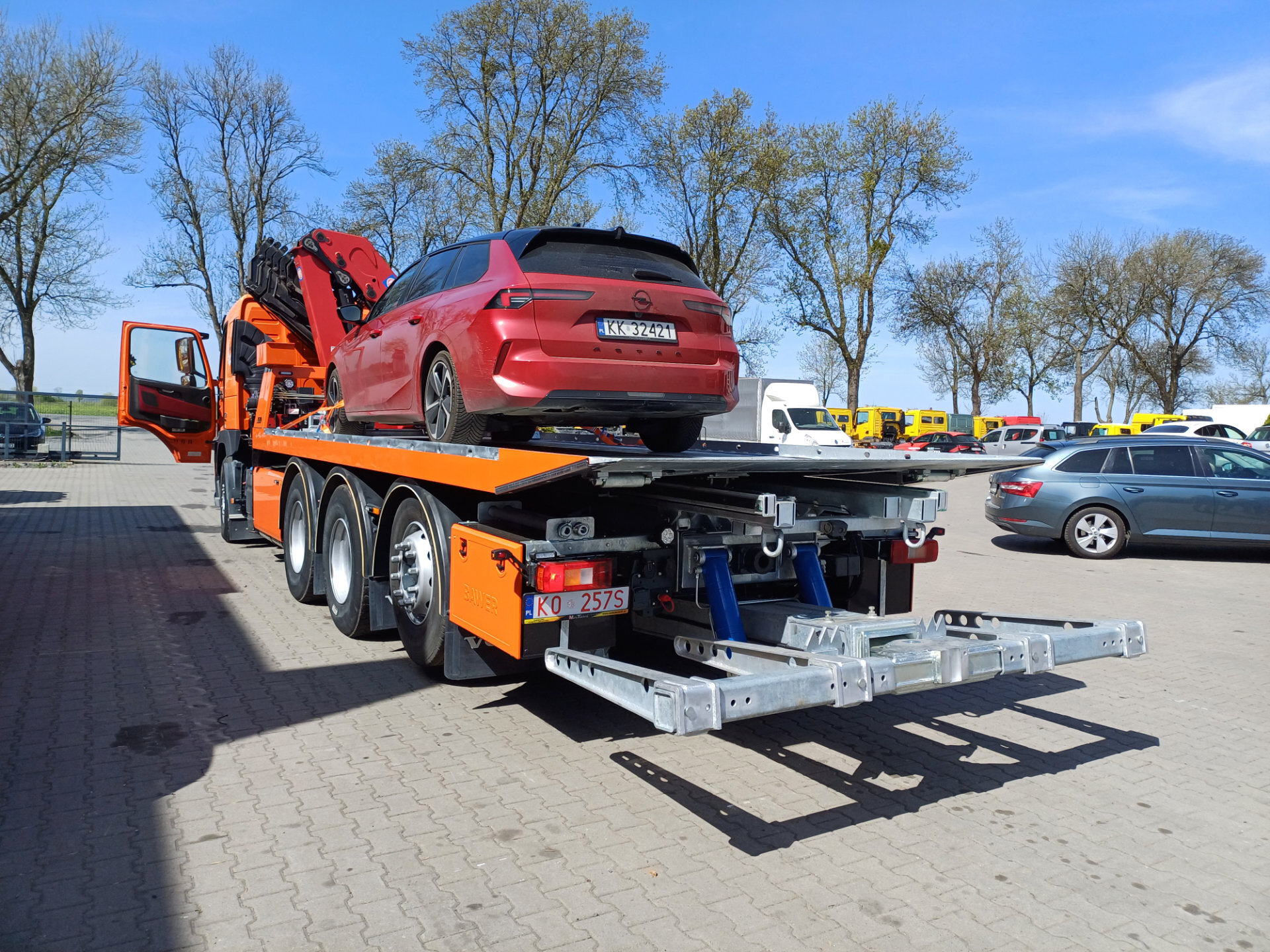 Pomarańczowy Volvo FM 450 z platformą hydrauliczną i czerwonym samochodem